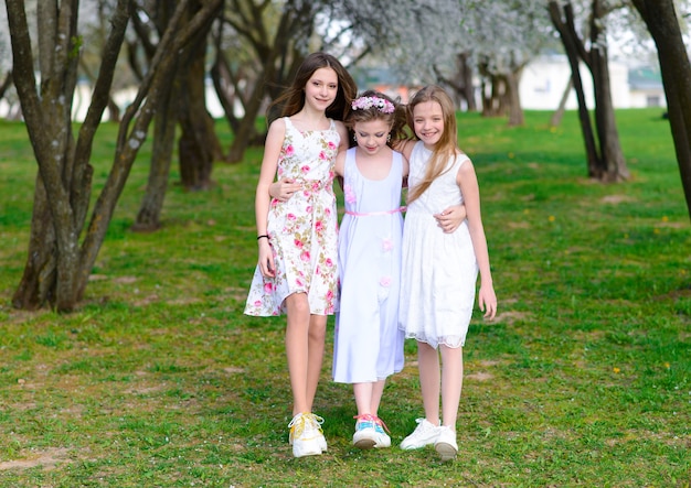 Tres adorables niñas en vestidos se dan la mano en un círculo tomados de la mano. Primavera, jardín.