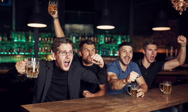 Tres aficionados al deporte en un bar viendo fútbol. Con cerveza en las manos