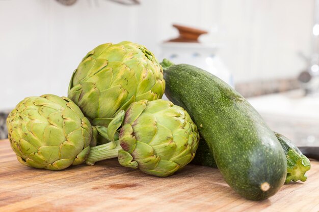 Três alcachofras de corpo redondo e várias abobrinhas agrupadas na cozinha legumes para preparação de guisados
