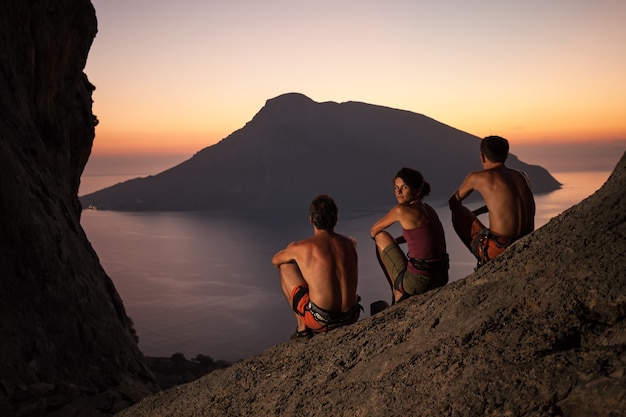 Três alpinistas usando cinto de segurança e descansando ao pôr do sol