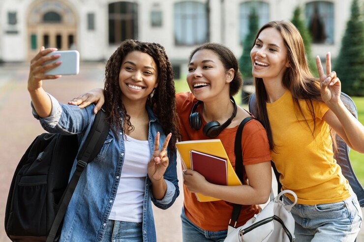 Foto três alunas multiétnicas falando selfie em smartphone ao ar livre