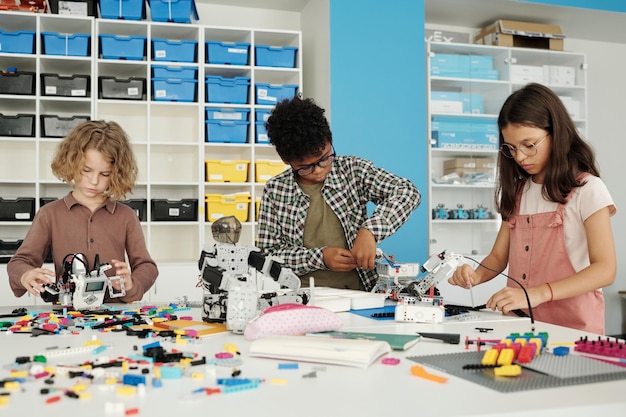 Três alunos inteligentes do ensino fundamental construindo novos robôs na aula