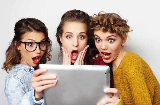 Foto três amigas adolescentes tirando selfie com tablet digital, estúdio filmado sobre fundo cinza