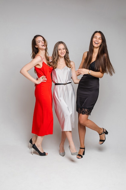 Tres amigas alegres en hermosos vestidos, aislados en la pared blanca