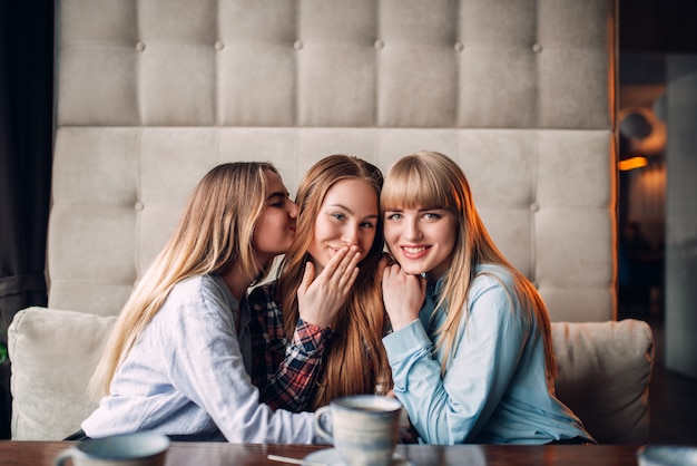 Tres amigas atractivas abrazos juntos en el café