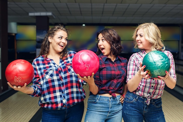 Tres amigas atractivas alegres sostienen bolas de boliche y se miran