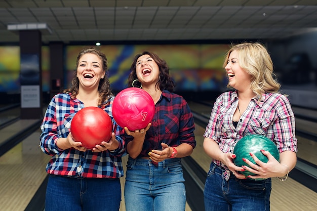 Tres amigas atractivas alegres sostienen bolas de boliche y se ríen.