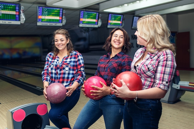 Três amigas engraçadas e atraentes pegam bolas de boliche.