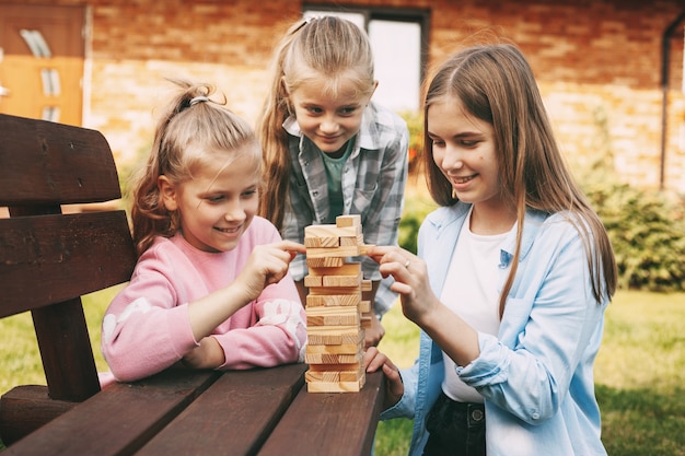 Três amigas jogam um jogo de tabuleiro de madeira ao ar livre perto de sua casa