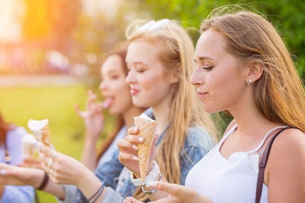 Três amigas jovens alegres em um passeio de pé em uma fileira sorrindo alegremente comem casquinhas de sorvete nas férias de verão. Fechar-se