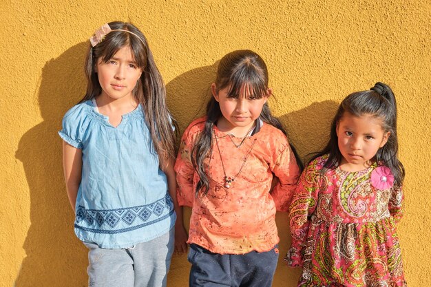 Foto tres amigas latinas en una pared amarilla mirando a la cámara en un soleado día de verano en américa latina bolivia