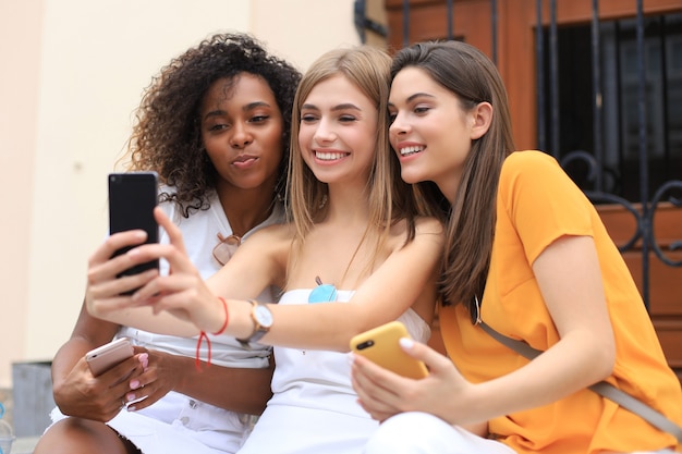 Tres amigas lindas que se divierten juntos, tomando un selfie en la ciudad.