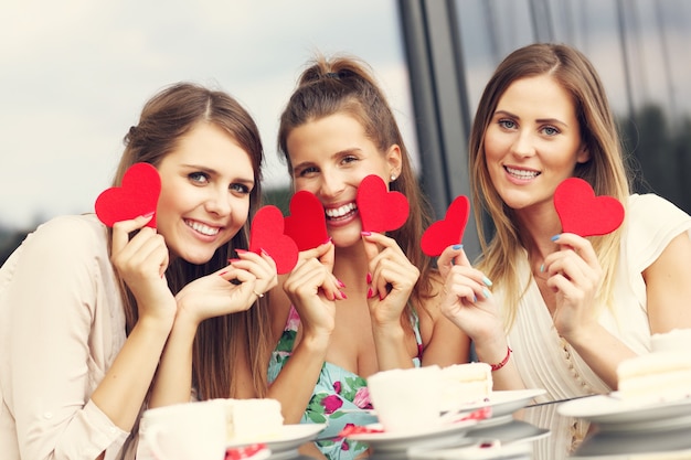 três amigas segurando corações em um café