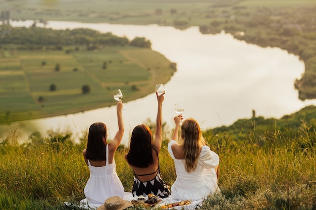 Tres amigas sentadas en el césped de la colina y divertirse.