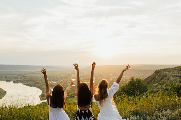 Foto tres amigas sentadas en el césped de la colina y divertirse.