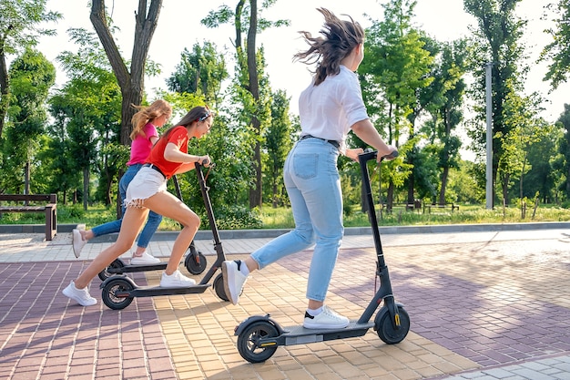 Tres amigas de vacaciones divirtiéndose conduciendo scooter eléctrico