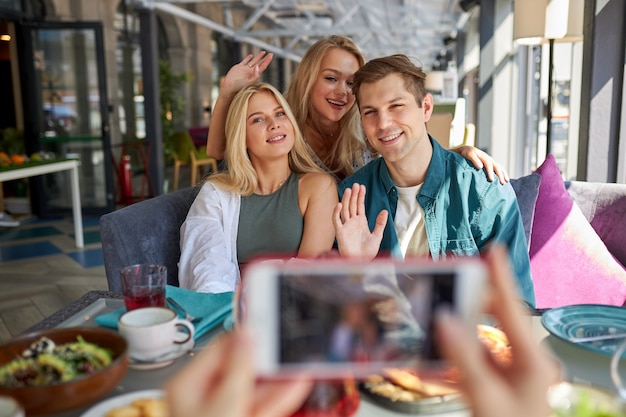 Três amigos caucasianos positivos posando para uma foto no smartphone