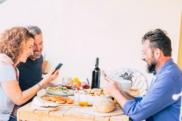 Tres amigos caucásicos comiendo en el restaurante cada uno mirando el teléfono y sin hablar con los demás