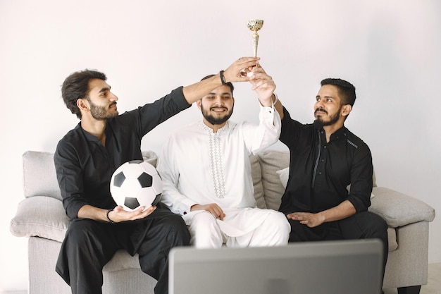 Três amigos do sexo masculino indianos sentados em um treinador enquanto assistem a uma partida de futebol no laptop