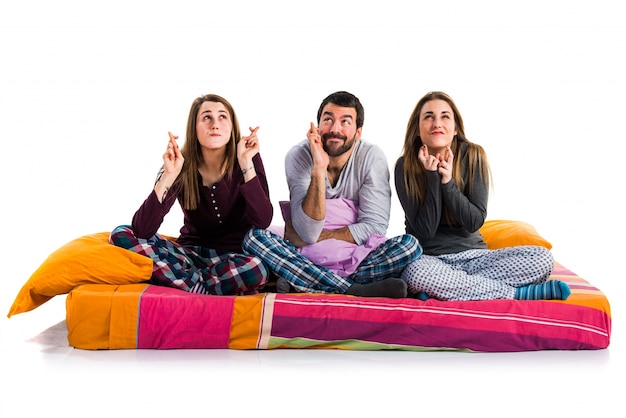 Foto três amigos em uma cama com os dedos cruzados