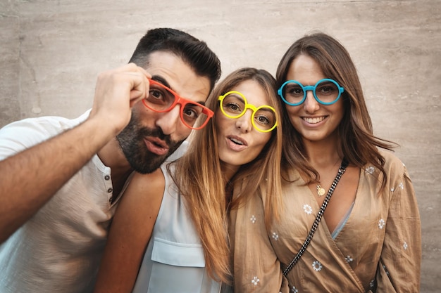 Três amigos estudantes engraçados olhando com óculos coloridos - Retrato de três jovens amigos olhando para a câmera