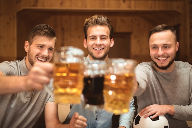 Los tres amigos felices tintinean vasos con una cerveza