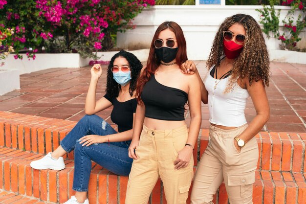 Três amigos latinos posando para a câmera no parque usando máscara protetora