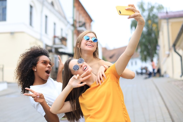 Três amigos lindos garotas se divertindo juntos, tirando uma selfie na cidade.