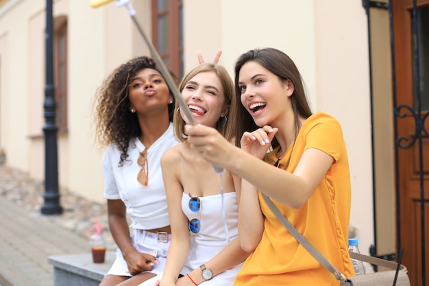 Três amigos lindos garotas se divertindo juntos, tirando uma selfie na cidade.