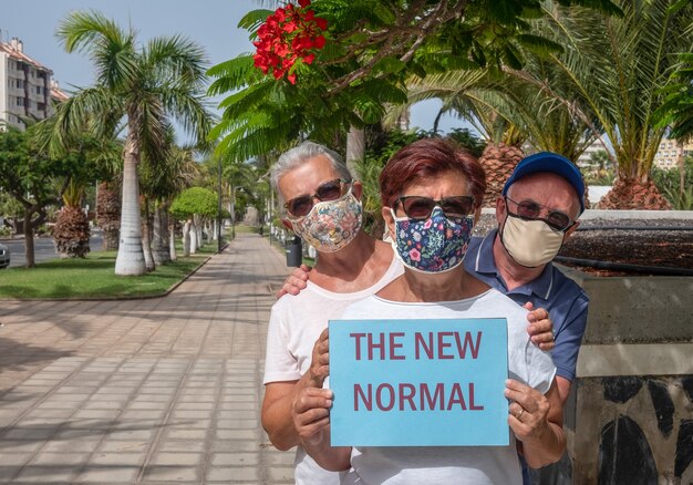 Tres amigos mayores disfrutan al aire libre en un parque público con mascarilla debido al coronavirus