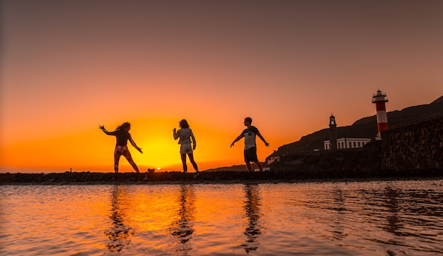 Três amigos no pôr do sol laranja nas salinas e ao fundo o Farol de Fuencaliente na rota dos vulcões ao sul da ilha de La Palma, nas Ilhas Canárias, Espanha