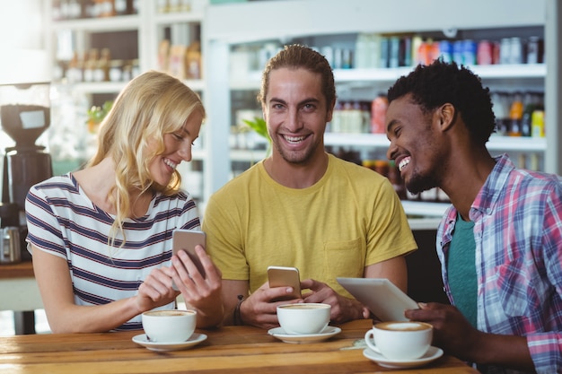 Tres amigos que usan teléfonos móviles mientras toman una taza de café