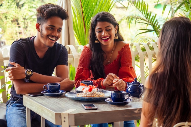 Tres amigos de ritmo indio comiendo panqueques dulces con té masala en un café de playa tropical de verano