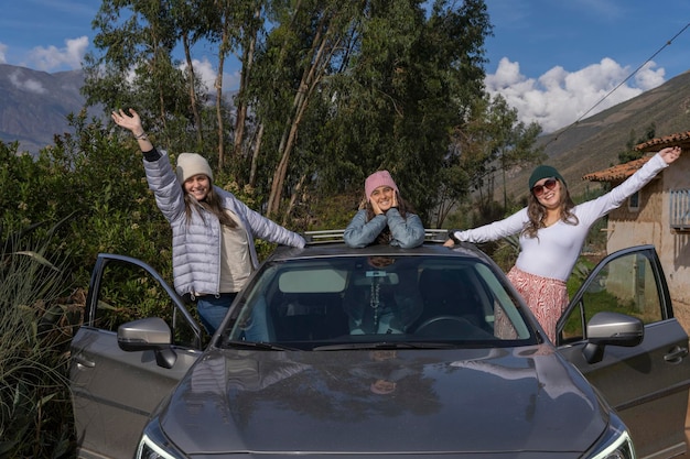 Três amigos saindo de um carro com os braços levantados nas montanhas