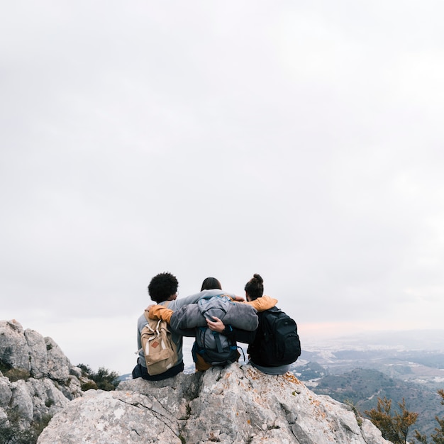 Três amigos sentados no topo da montanha, apreciando a vista