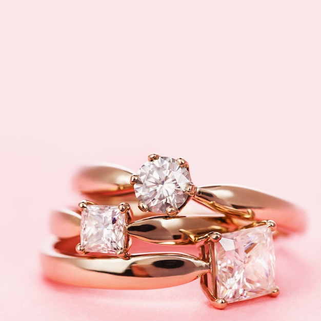 Três anéis de noivado com diamantes em um fundo rosa e espaço de cópia