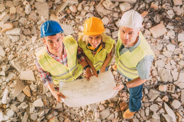 Tres arquitectos constructores revisan el plan del edificio dañado por el desastre. Mirando a la cámara.