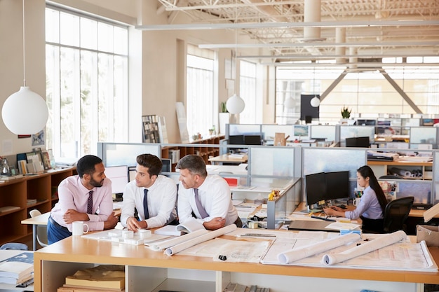 Tres arquitectos masculinos discutiendo en una oficina abierta