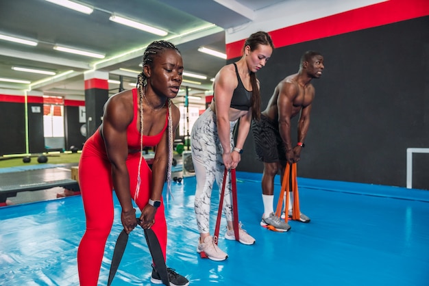 Três atletas multirraciais fisiculturistas fazendo exercícios de tonificação com elásticos em uma academia de torso. dois fisiculturistas africanos e um caucasiano fazendo uma rotina de exercícios de crossfit