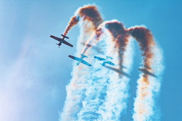 Tres aviones de motor ligero realizan acrobacias aéreas: un bucle muerto. El sol brillante ilumina los aviones y las sombras caen sobre el humo que dejan en el cielo.