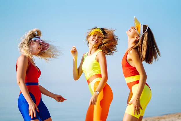 Tres bailarinas jóvenes bailando en trajes de baño brillantes en la playa deporte fitness vida activa