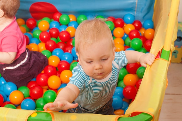 Três bebês brincando com bolinhas multicoloridas dentro do cercadinho