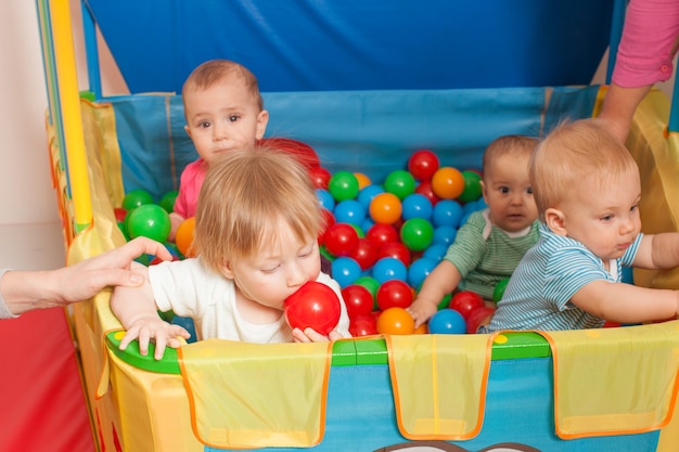 Três bebês brincando com bolinhas multicoloridas dentro do cercadinho