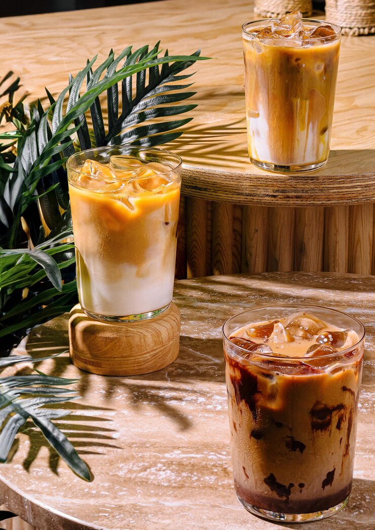 Tres bebidas de café helado sentadas en una mesa de café al sol