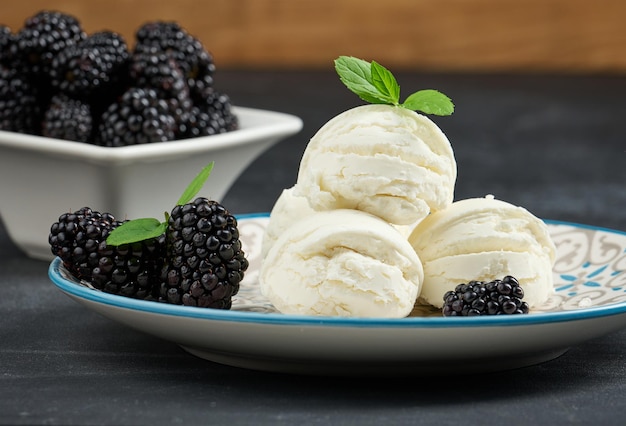 Tres bolas de helado blanco en un plato redondo con hojas de menta sobre una mesa negra