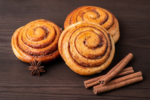 Tres bollos de canela en la mesa de madera con algunas ramas de canela. Panadería casera sabrosa