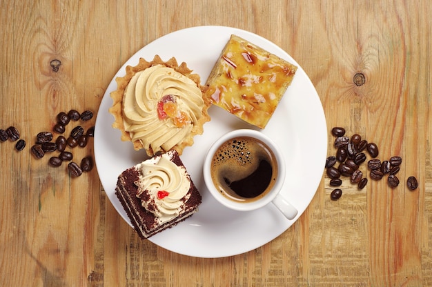 Três bolos e uma xícara de café em chapa branca na velha mesa de madeira, vista superior
