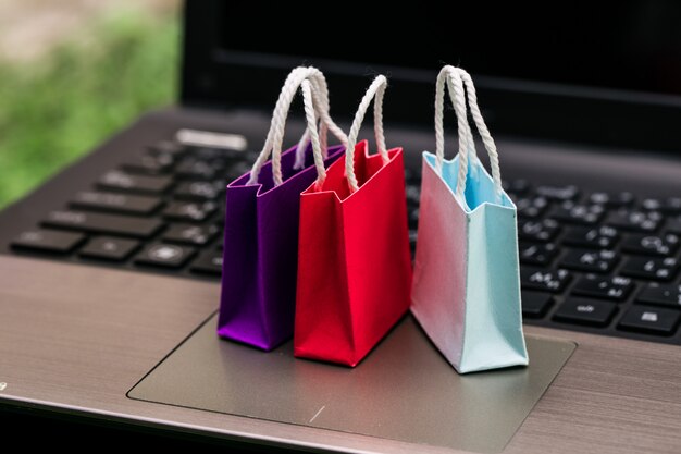 Tres bolsas de papel de colores en el teclado del ordenador portátil. Ideas sobre compras en línea. El comercio electrónico o el comercio electrónico es una transacción de compra o venta de bienes o servicios en línea a través de Internet.