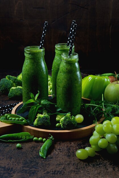 Tres botellas del batido verde más útil de vegetales y frutas se encuentran en una pared de madera en el centro, y alrededor de vegetales y frutas verdes. Foto vertical. Vista superior.