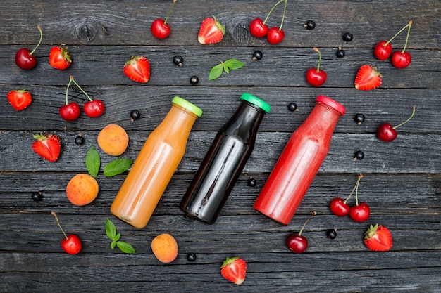 Tres botellas de jugo y frutas en la mesa de madera negra. Concepto de comida